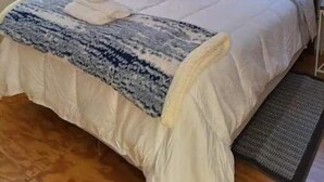A bedroom with a bed, a bedside lamp, and a window with blinds. - Restful manufactured suite where visitors can relax during their stay.  (Hinesville)