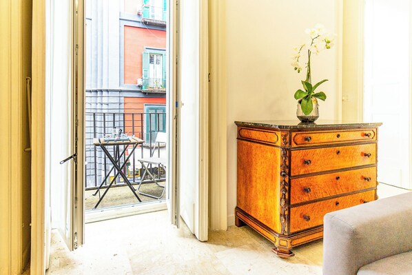 A room with a sliding glass door leading to an outdoor area with a table and chairs. There is a wooden dresser with drawers and a vase with flowers on top.