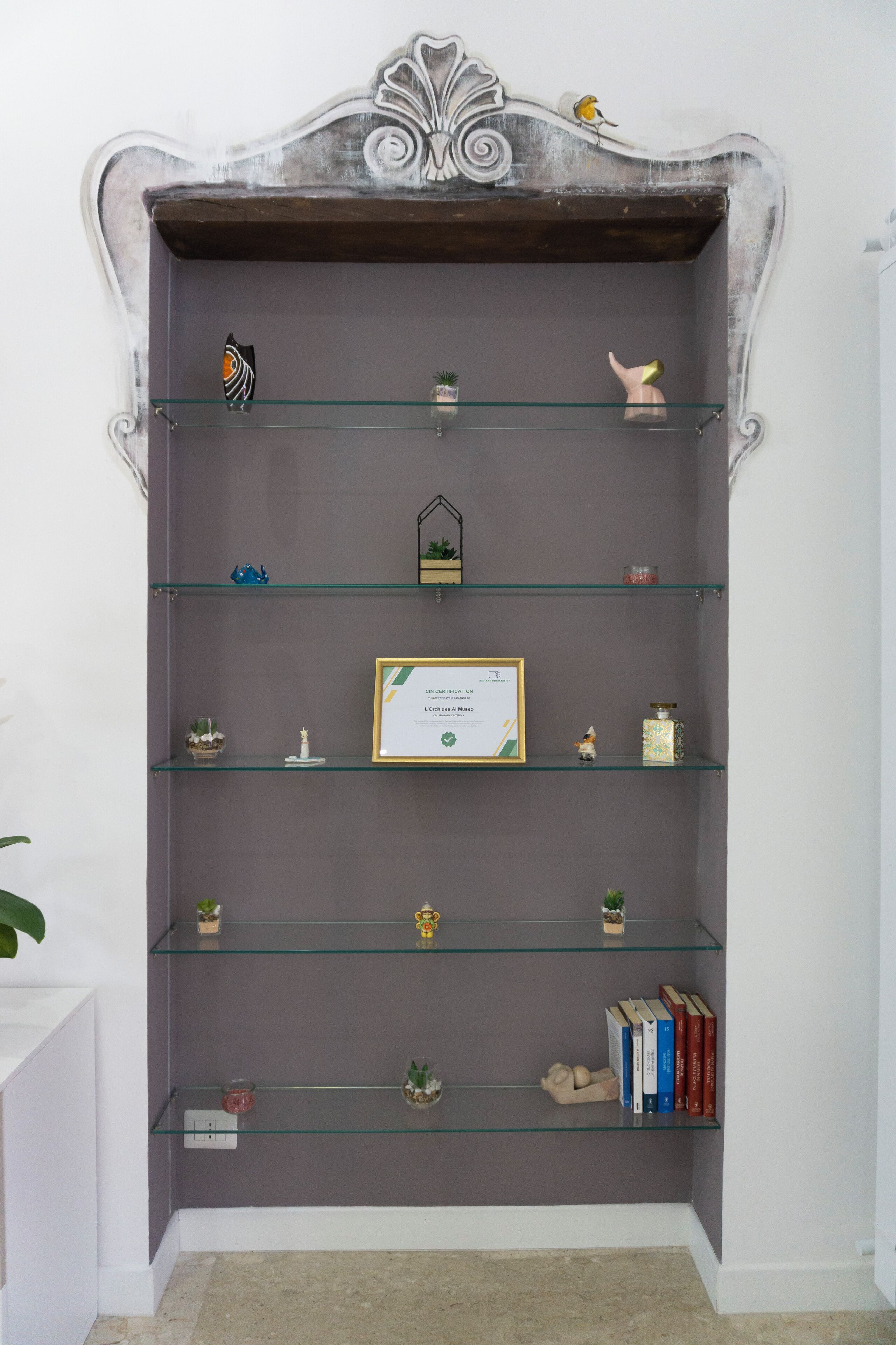 A wall-mounted display with multiple shelves containing various decorative items, a framed certificate, and a small bird figurine.