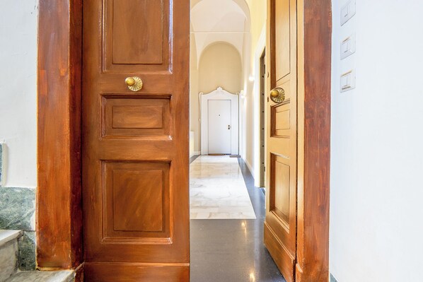 Une porte en bois dotée d’une poignée en laiton, qui donne sur un couloir au sol en marbre et aux murs blancs.
