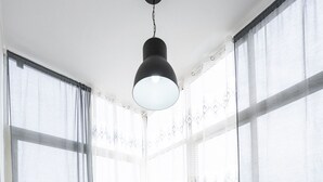 A spacious room with large windows, a hanging light fixture, and a wooden floor.