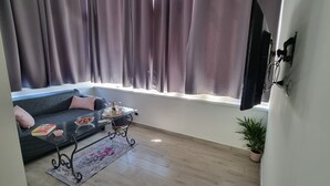 A living room with a sofa, a glass coffee table, a potted plant, and a window with curtains.