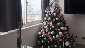 A living room with a glass coffee table, a Christmas tree, and a flat-screen TV.