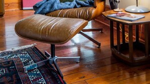 A cozy room with a wooden floor, a pink door with glass panels, a brown leather chair with a green pillow, a small round table with a lamp, and a patterned rug. - Silk Stocking District historical mid-century home (Galveston)