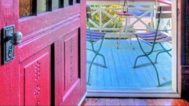 A colorful wooden door leading to a balcony with a view of a blue house and palm trees. - Silk Stocking District historical mid-century home (Galveston)