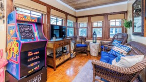 Quarto com máquina de arcade Pac-Man, móveis de vime e uma televisão.