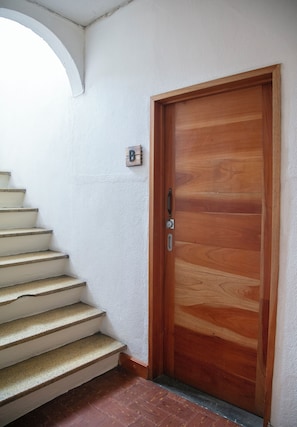 Eine Holztür mit einem Metallgriff, eine weiße Wand und eine Treppe mit beigen Stufen.