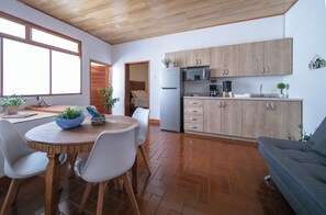 Una cocina moderna con armarios de madera, un refrigerador y un microondas. Hay una mesa de comedor con sillas y una planta en maceta.
