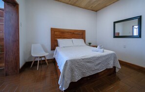 Une chambre à coucher avec une tête de lit en bois, un lit blanc, une chaise blanche, une petite table de chevet et un miroir accroché au mur.