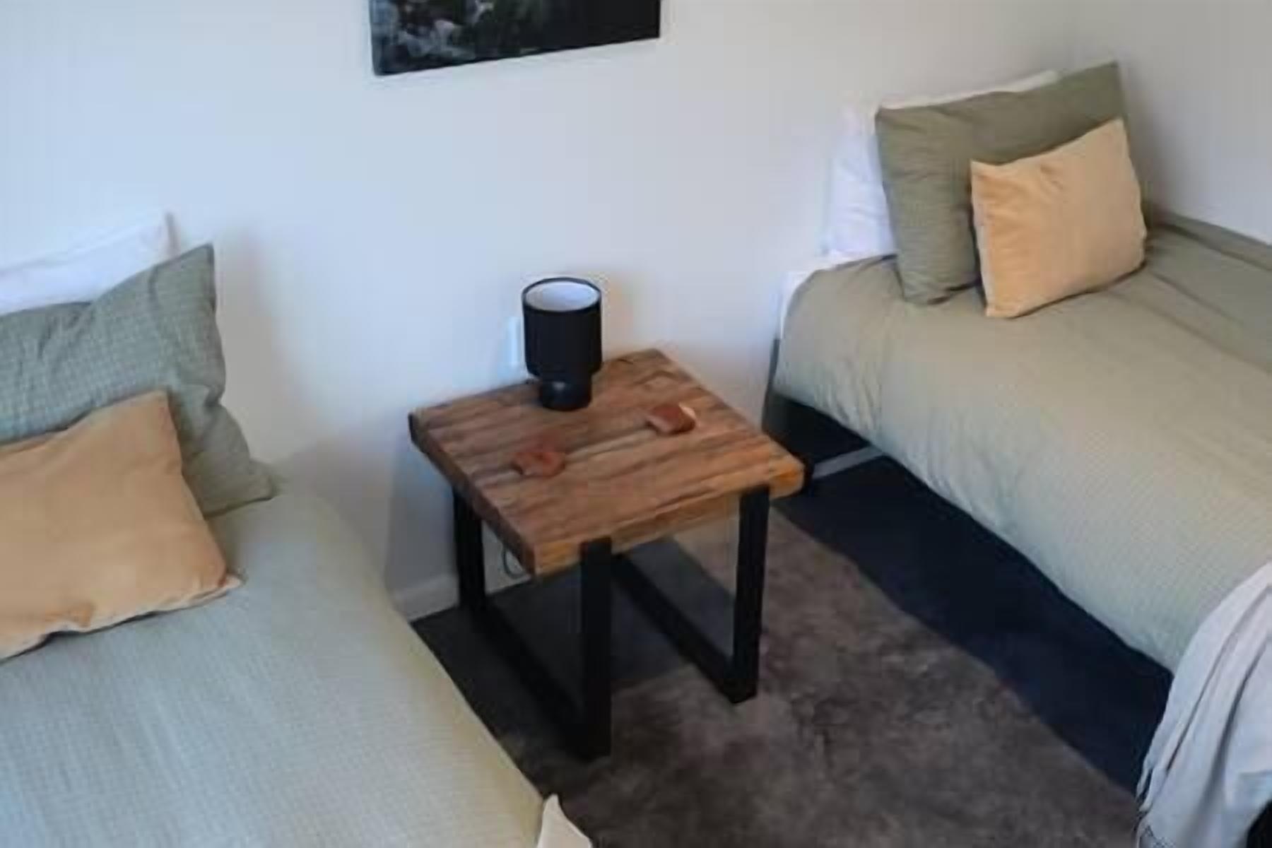Ett litet rum med två sängar, den ena med ett grönt täcke och den andra med ett beige täcke. Där står ett träbord med ett svart föremål på, troligen en högtalare eller en telefon.