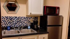 A compact kitchen with white cabinets, a black countertop, a microwave, and a stainless steel refrigerator.