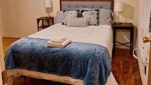 A bedroom with a bed, two bedside tables, a nightstand, a wooden floor, and a ceiling light.