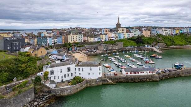 Uma cidade costeira com edifícios coloridos, uma torre de igreja e uma marina com barcos.