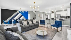 Ein modernes Wohnzimmer mit einem grauen Sofa, blauen Sesseln, einem Glastisch und einer Treppe mit einem geometrischen Wanddesign.