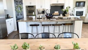 A modern kitchen with white cabinets, a central island with bar stools, and a wooden countertop. - Santa Clarita Tropical Paradise, Six Flags Magic Mountain, LA, Beaches Drivable (Santa Clarita)