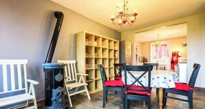 A dining area with a table set for four, surrounded by chairs with red cushions, a bookshelf, and a chandelier.