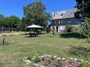 A stone house with a grassy yard, a picnic table, and a swing set.