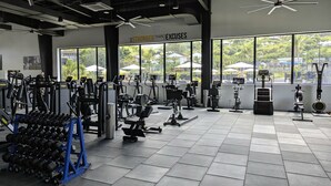 Un gimnasio con diverso equipo de ejercicio, ventanas amplias y una frase motivacional en la pared.