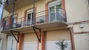 Un edificio residencial de varios pisos con un balcón, una motocicleta estacionada al frente y una planta en maceta.