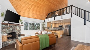 A modern living room with a stone fireplace, a leather sofa, and a wooden ceiling.