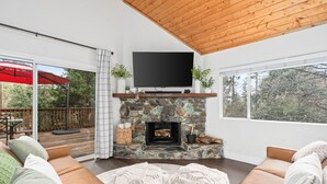 A cozy living room with a stone fireplace, a flat-screen TV mounted above it, and a comfortable seating area with cushions.