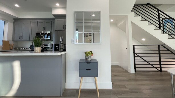 A modern kitchen with grey cabinets, a central island, and a small side table with a plant.