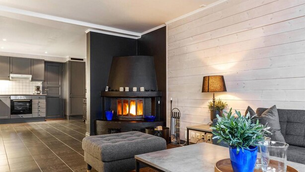 Ett modernt vardagsrum med en öppen spis, en grå soffa och en matplats med ett bord och stolar.