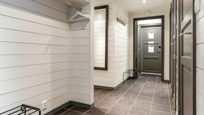 En hall med vitmålade panelväggar, en mörk dörr och ett klinkergolv.