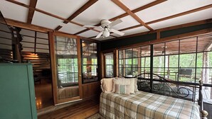 A bedroom with a plaid bedspread, a ceiling fan, and large windows offering a view of the outdoors.