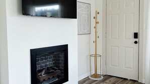 A room with a flat-screen TV mounted on the wall, a fireplace below it, and a wooden floor.