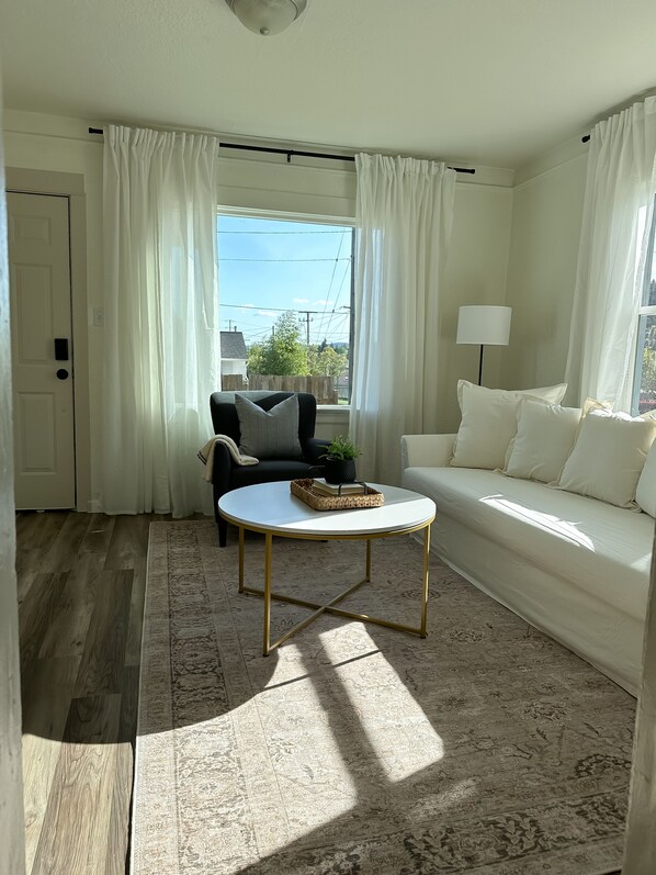 A living room with a white sofa, a black armchair, a round coffee table, and a lamp.