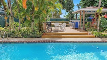 Relax by the serene pool surrounded by lush greenery and a wooden deck.