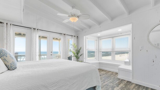 Ein Schlafzimmer mit einem großen Bett, einem Deckenventilator und Blick auf den Strand durch große Fenster.
