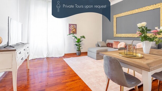 A modern living room with a wooden dining table, grey sofa, and a large mirror. - Daplace - Alma Apartment (Roma)