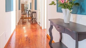 A hallway with wooden flooring, a dark console table with a vase of flowers, and a blue accent wall. - Daplace - Alma Apartment (Roma)