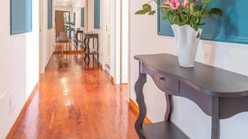 Un couloir doté d’un parquet en bois, une console sombre ornée d’un vase de fleurs et un mur d’accent bleu.