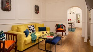 A living room with a yellow sofa, a glass coffee table, and a wooden armchair. - Daplace - Flaminia Apartment (Roma)