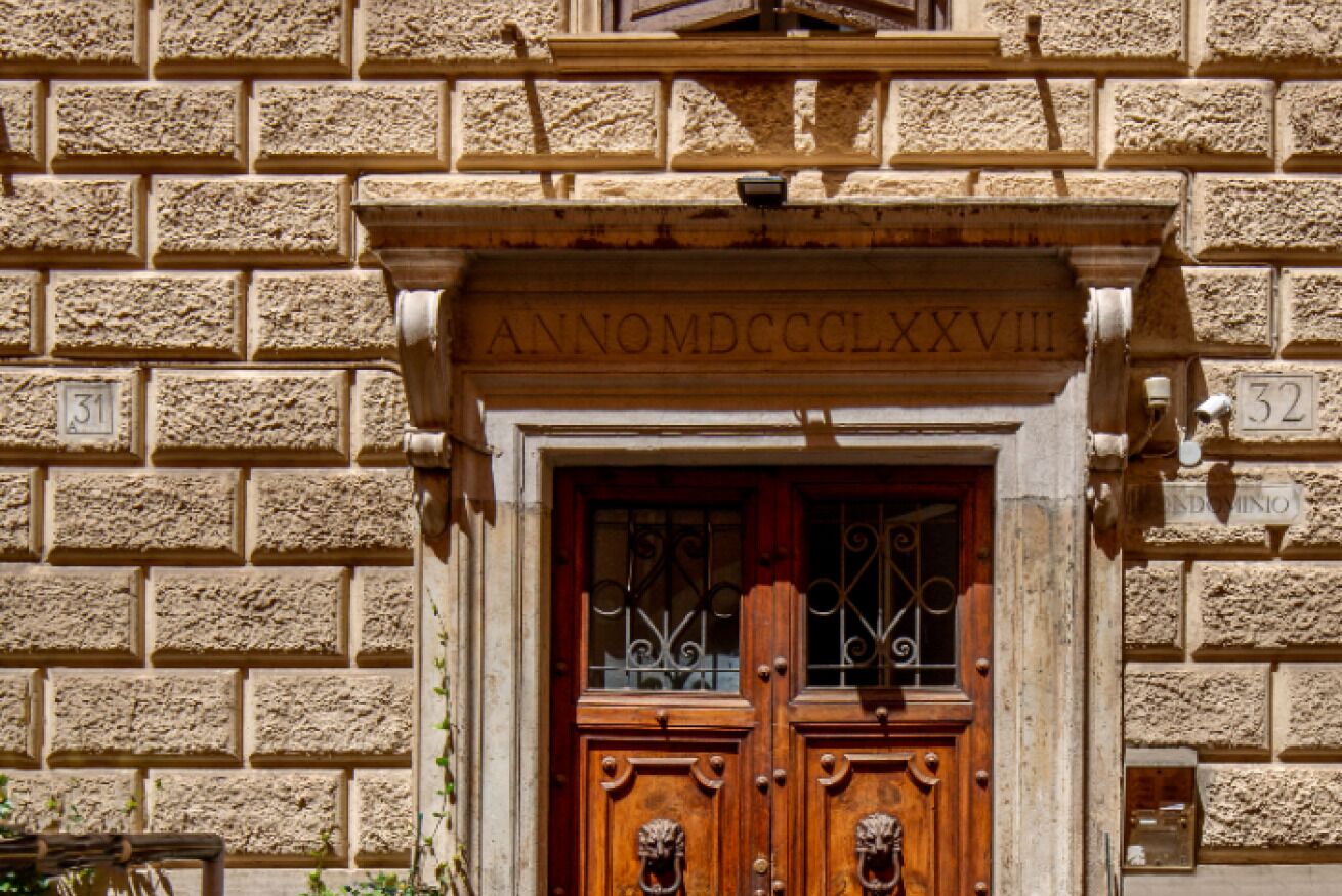 A building facade with a stone wall and a wooden door with a metal gate. - Daplace - Flaminia Apartment (Roma)