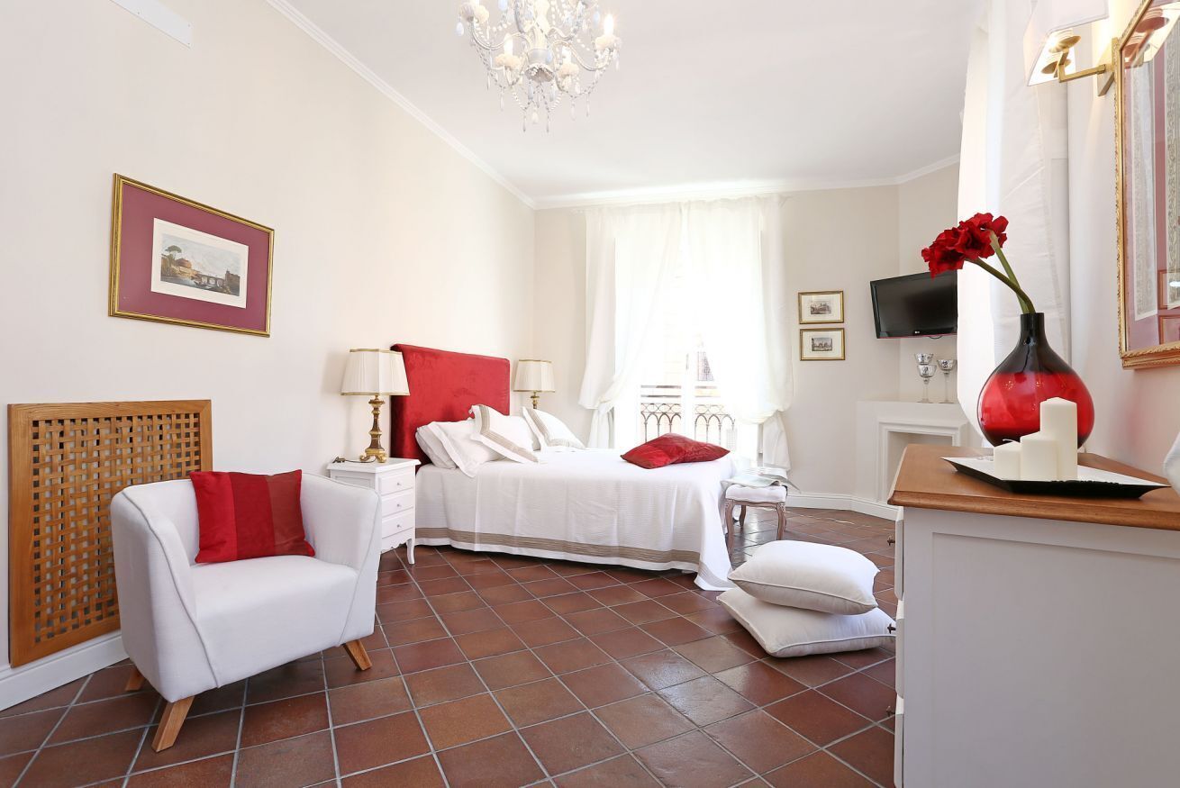Una habitación de hotel con una cama, una silla, un escritorio, un televisor y un florero con flores.