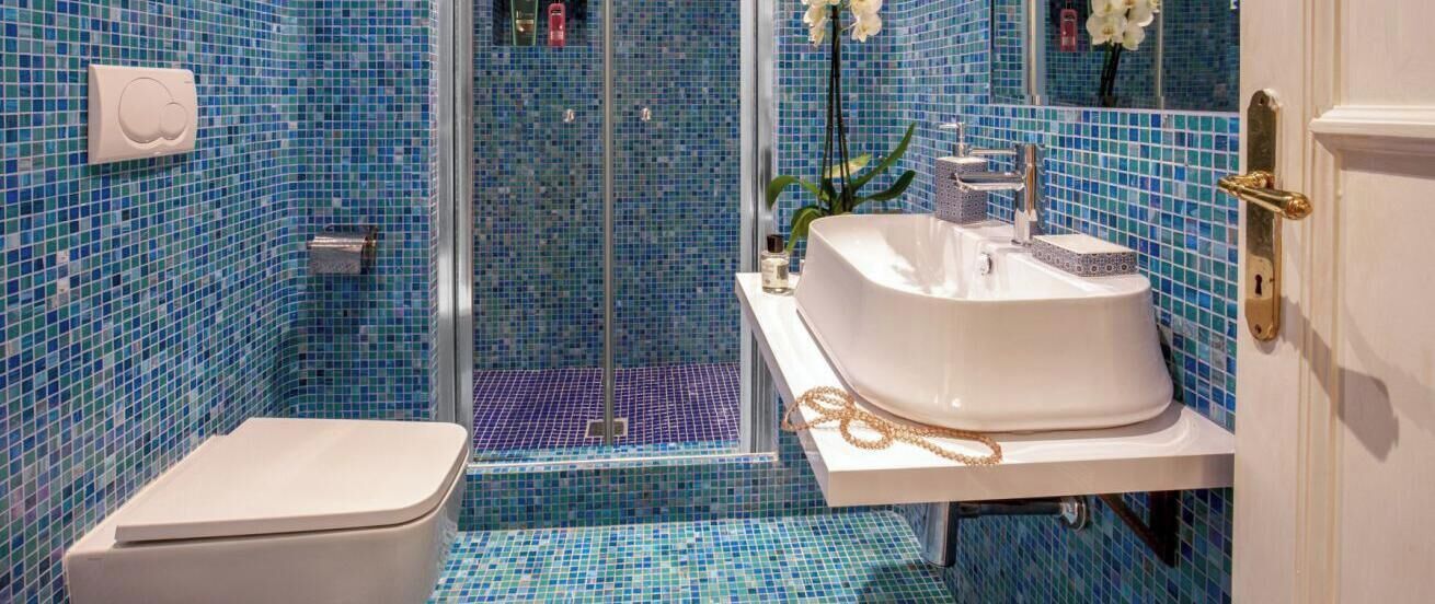 A bathroom with a white sink, a toilet, and a shower area with blue mosaic tiles.