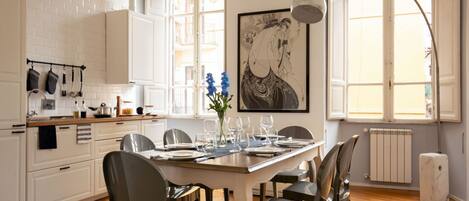 Une cuisine moderne avec des meubles blancs, une table à manger pour quatre personnes et une grande fenêtre offrant une belle vue.