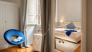 Quarto com cama, poltrona, mala e lustre.