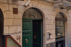 A building facade with numbered doors, a security camera, and a window with a sign.