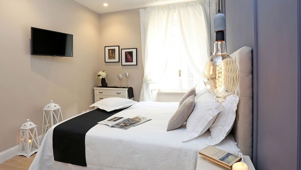 A modern bedroom with a bed, bedside table, lamp, and a flat-screen TV mounted on the wall. - Daplace - Lucrezia Apartment (Roma)