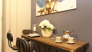 A dining area with a wooden table, chairs, a vase of flowers, a candle, a pitcher, and a painting on the wall. - Daplace - Lucrezia Apartment (Roma)