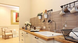 A modern kitchen with a wooden countertop, white cabinets, and a large sink. There are hanging pots and pans, a dish rack, and a potted plant on the counter. - Daplace - Lucrezia Apartment (Roma)