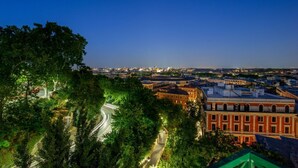 Une vue nocturne d’une ville, avec un bâtiment rouge imposant, une route sinueuse et une végétation luxuriante.