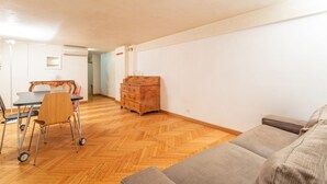 Ein Wohnzimmer mit Holzdielen im Fischgrätmuster, einem grauen Sofa und einer Holzkommode.