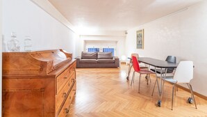 Ein geräumiges Zimmer mit einem Holzkapfen, einem grauen Sofa, einem Esstisch mit St ühlen und einem Fenster mit Jalousien.