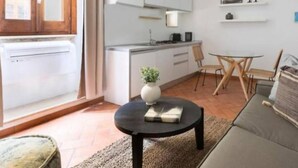 A modern living room with a sofa, a coffee table with a book and a plant, a dining area with a table and chairs, and a kitchen area with cabinets and a refrigerator. - Daplace - Emilia Apartment (Roma)